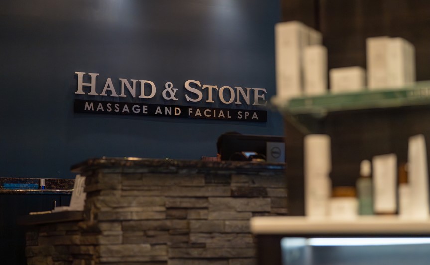 A softly lit Hand & Stone Massage and Facial Spa lobby, including the stone counter and logo.